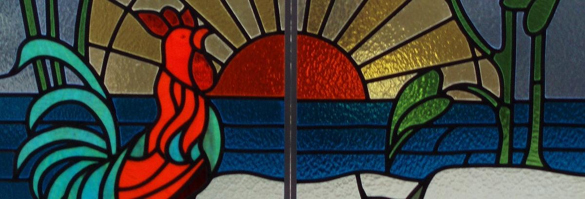 Een haan, ondergaande zon en bloem in glas in lood